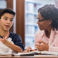 Black female teacher working one-on-one with Latino middle school student on fluency