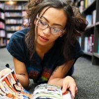 Mixed race high school girl laying on floor of library reading graphic novels