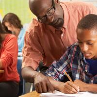 Black male high school teacher helping Black male student in class