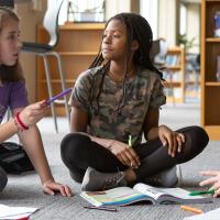 Three middle school girls sitting on floor of school library talking about schoolwork