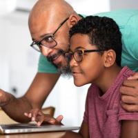Father and middle school son looking at laptop together at home
