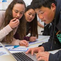 Three multicultural high school students using laptops for class project