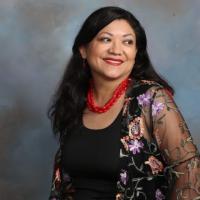 Picture of Reyna Grande looking to the side with a red, coral necklace and floral overlay wrap.