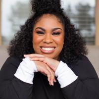 Author Angie Thomas smiling at the camera with her hands under her chin