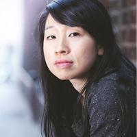 Elsie stares into the camera while leaning against a brick wall.