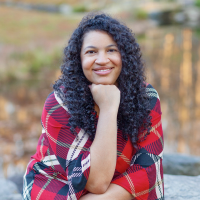 Michelle wearing a red, plaid dress smiling at the camera with her hand under her chin
