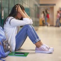 Middle grade student slouched against her locker with her hands in her hair and her knees pulled up.