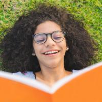 girl laying on grass reading an orange book