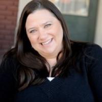 Head shot of Jennifer Brown in a black shirt sitting on the stoop of a brick house.