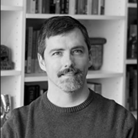 black and white picture of the author sitting in front of a bookcase behind him