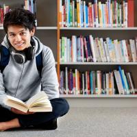 Teenage boy reading a book sitting in a library