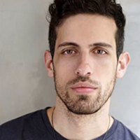 Adam looks into the camera for a head shot against a white wall.