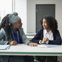 African American teacher and student sit at desks to discuss school work