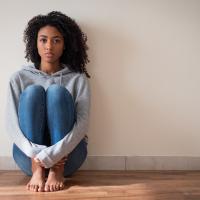 Young woman leaning against a blank wall hugging her legs.