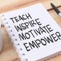The words teach, inspire, motivate, and empower written on a notepad next to a pen and a cup of coffee