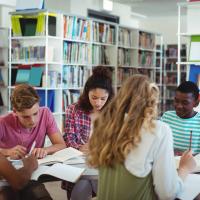 Group of teens studying at a table reading and writing