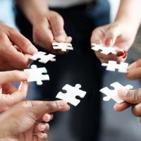 Seven peoples hand in a circle with white puzzle pieces