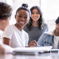 Group of teens sitting at a table and smiling while looking at their notebooks together