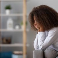 Adolescent girl looking sadly at the floor as she sits on a couch.