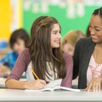 Teen and teacher smiling at one another as they sit together in the classroom