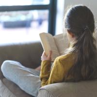 Teen girl reading on a couch not facing the camera