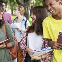 Three diverse students walking together holding books.