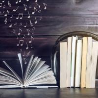 Book open with music notes floating above it, sitting next to a stack of books