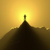 Person standing alone at the top of a mountain with the sun shining behind them.