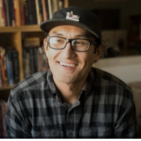 Head shot of illustrator Zeke Pena against a backdrop of books