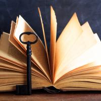 Large, old key laying against an open book sitting on a table.