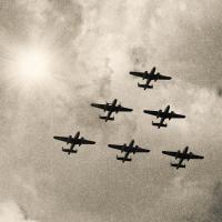 Five WWII bomber planes flying through the sky in a triangle formation